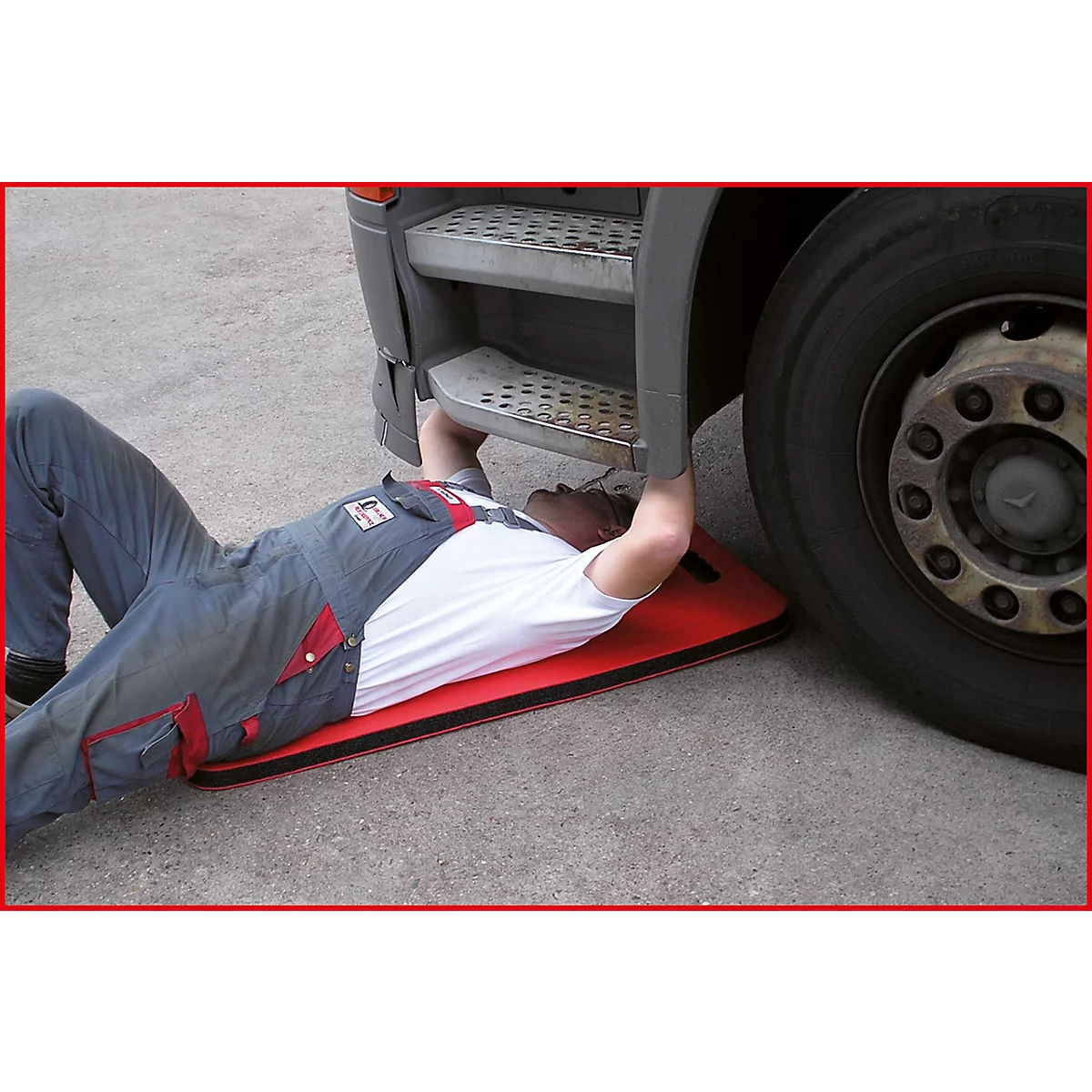 Ein Mann liegt unter einem LKW, auf einer roten Matte. Er arbeitet an der Unterseite des Fahrzeugs.